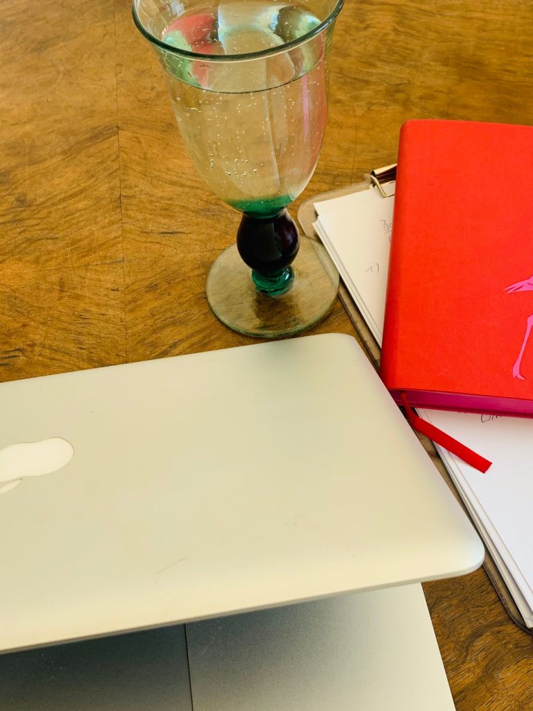 Laptop auf Holztisch, dabeneb Wasserglas, Block und rotes Notizbuch
